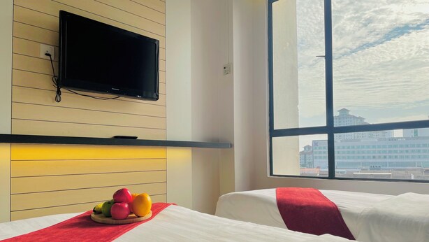 A hotel room with two beds, a flat-screen TV mounted on the wall, a fruit basket on the nightstand, and a large window offering a city view. - La Boss Hotel (Malacca City)