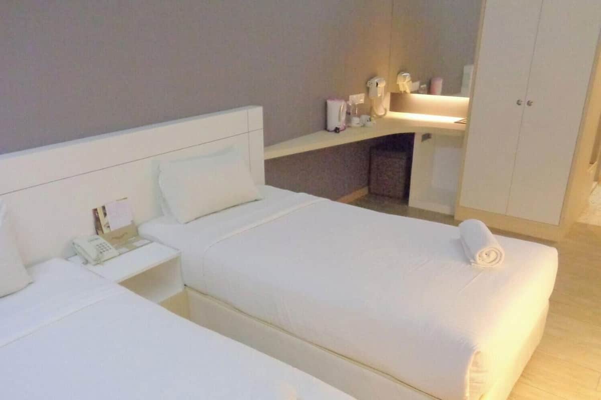 A hotel room with two beds, a bedside table with a phone, a small table with toiletries, and a cabinet with a mirror.