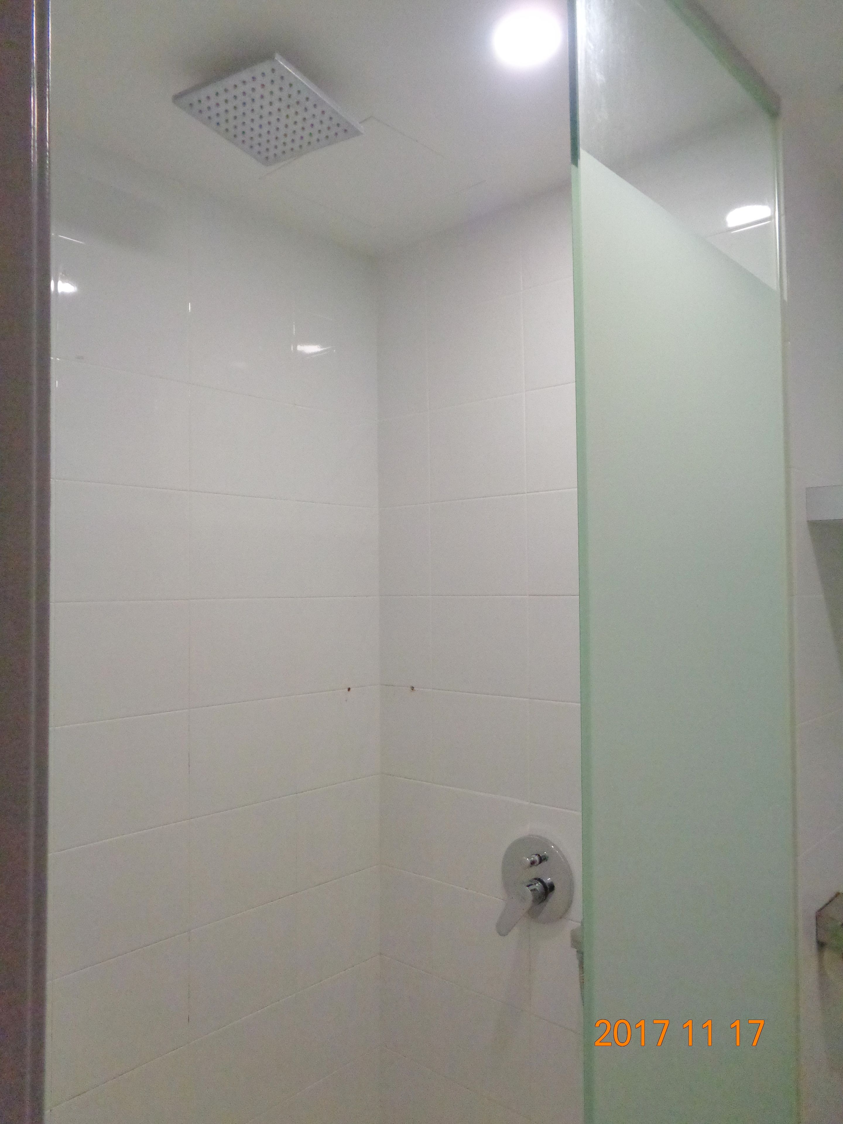 A shower with white tiles, a glass partition, and a ceiling vent.