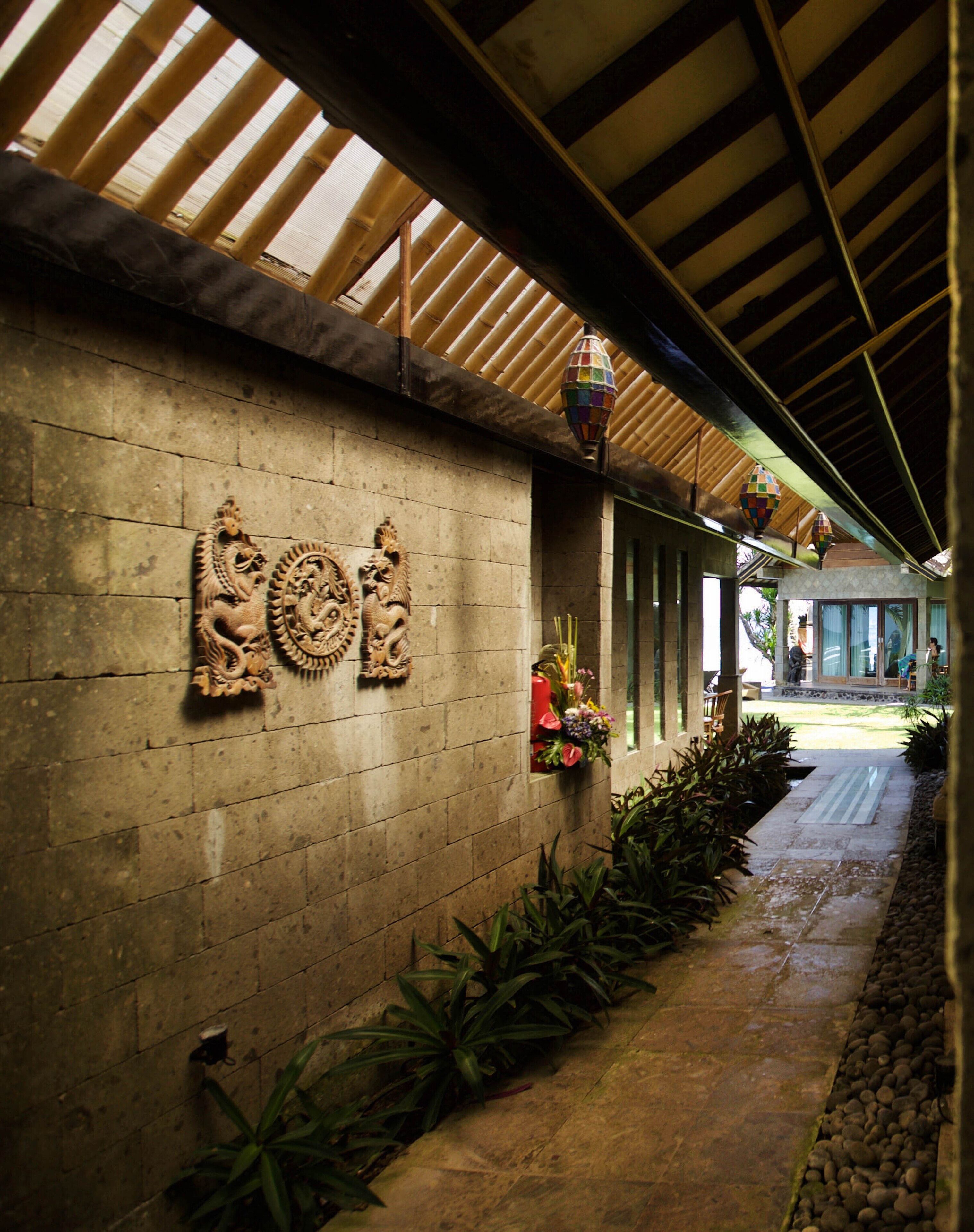 Un pasillo cubierto con pared de piedra decorada con figuras de leones tallados, suelo de baldosas y plantas en macetas.