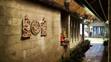 Un pasillo cubierto con pared de piedra decorada con figuras de leones tallados, suelo de baldosas y plantas en macetas.
