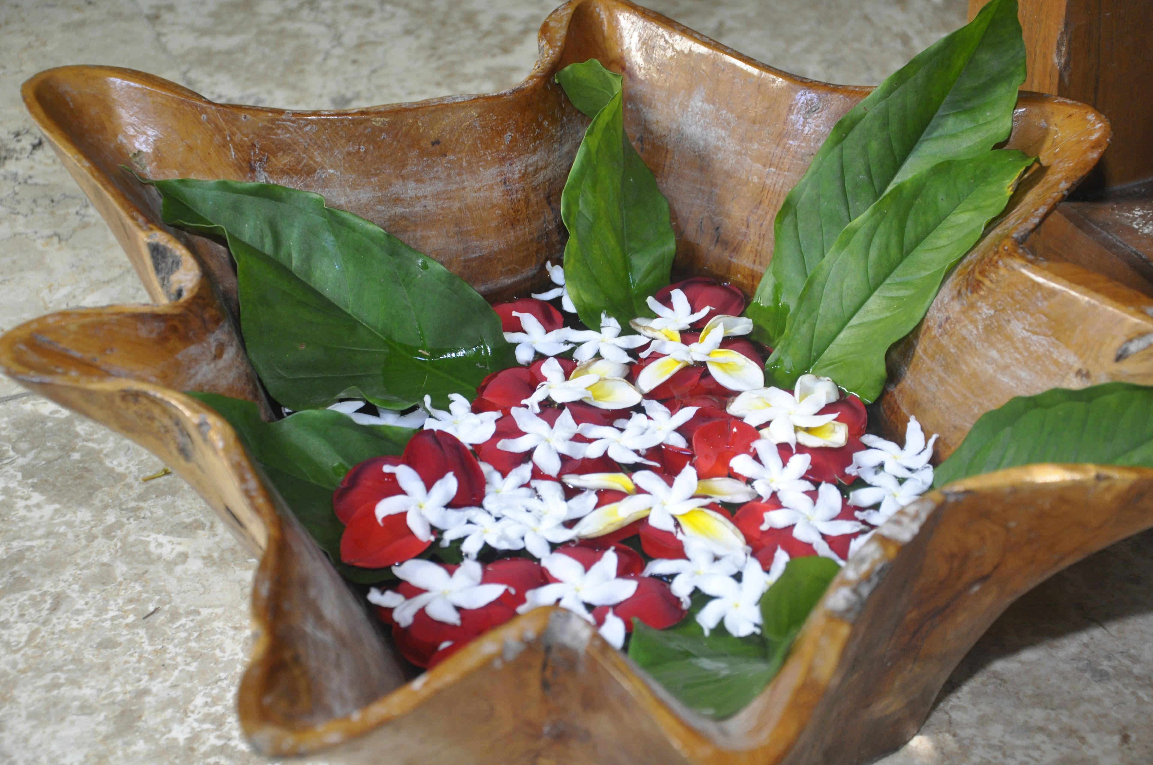 A wooden bowl filled with red flowers and green leaves.