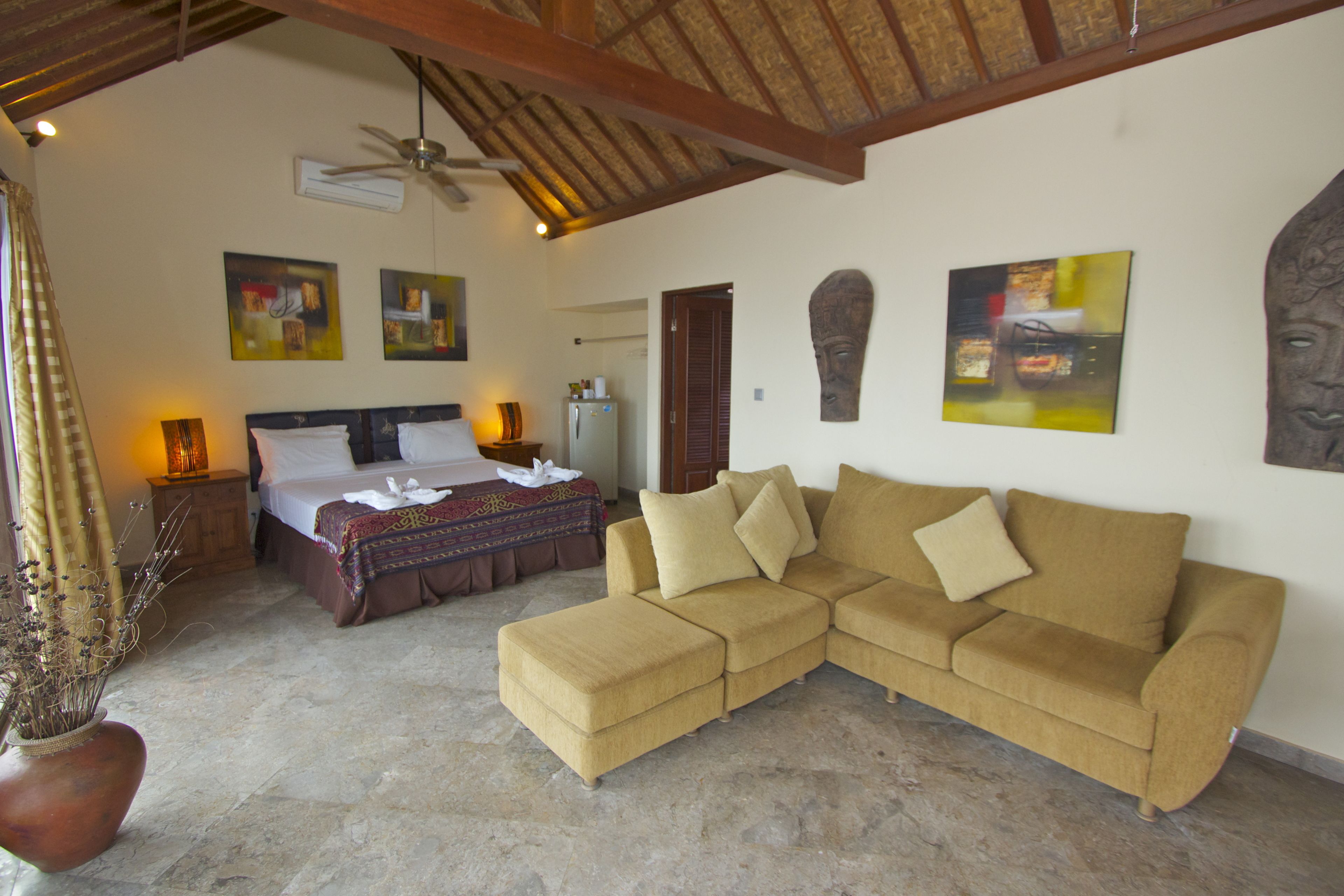 A bedroom with a bed, a sofa, a ceiling fan, and artwork on the walls.