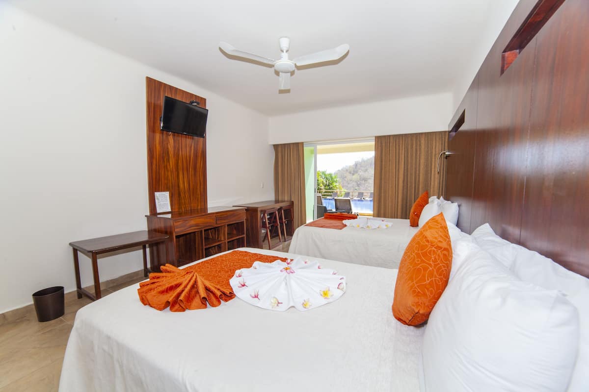A hotel room with two beds, a desk, a chair, a TV, and a view of the outdoors.