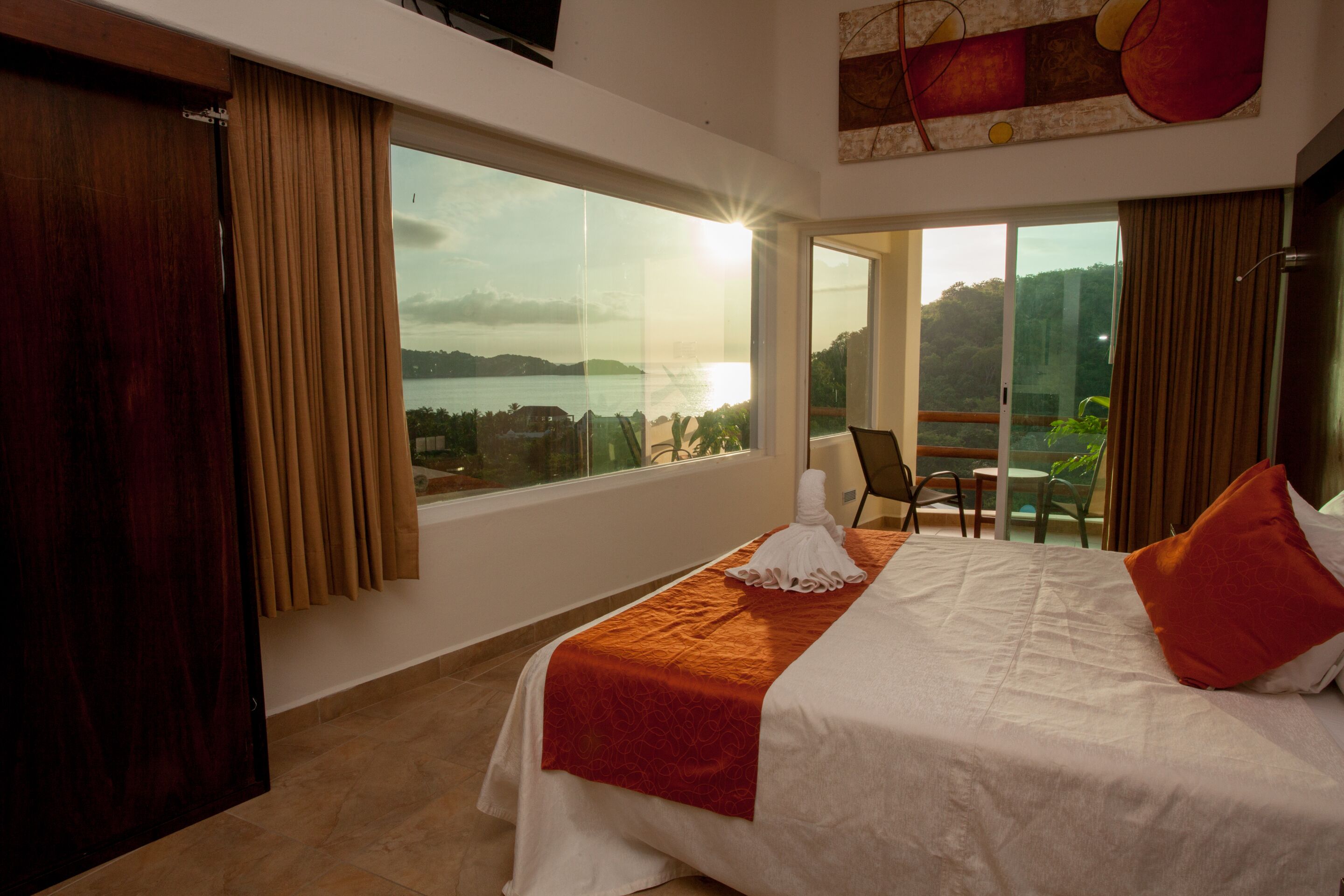 Una habitación de hotel con cama, vistas al mar, balcón y zona de comedor.