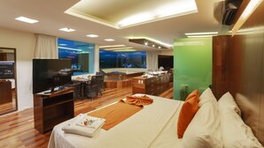 Habitación de hotel con una cama grande, televisión, escritorio con silla, sofá y vista a la ciudad de noche.