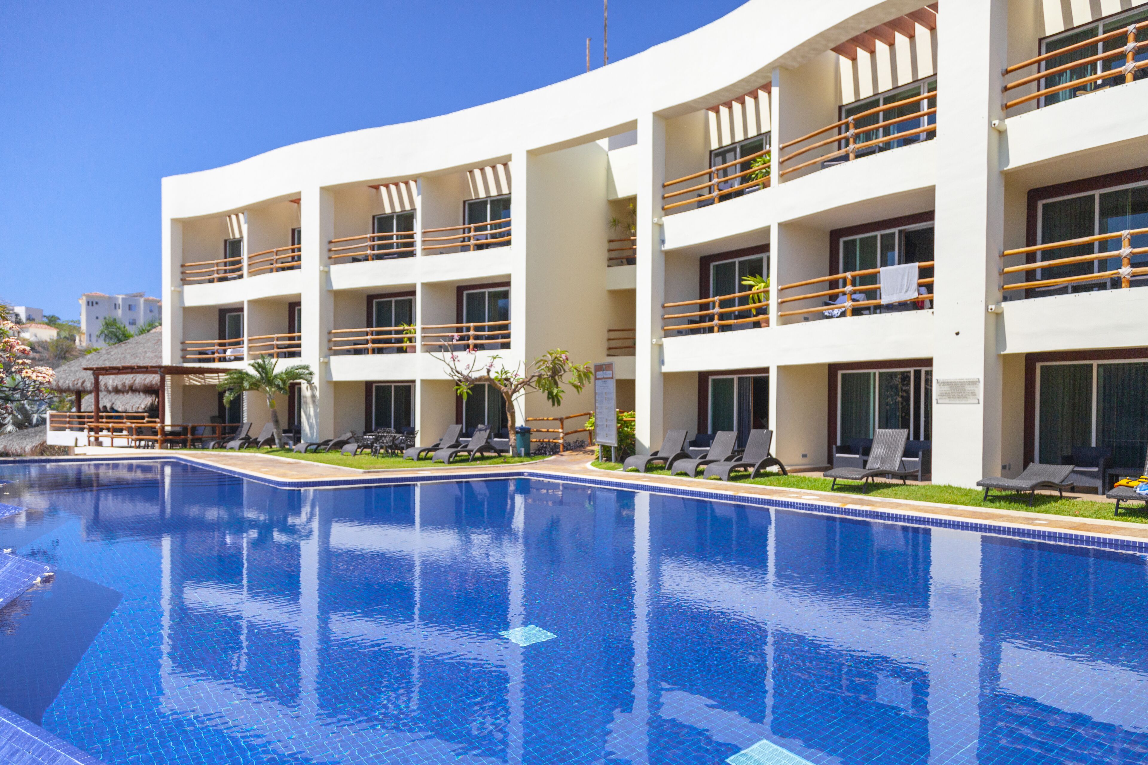 A hotel with a swimming pool, multiple balconies, and sun loungers.