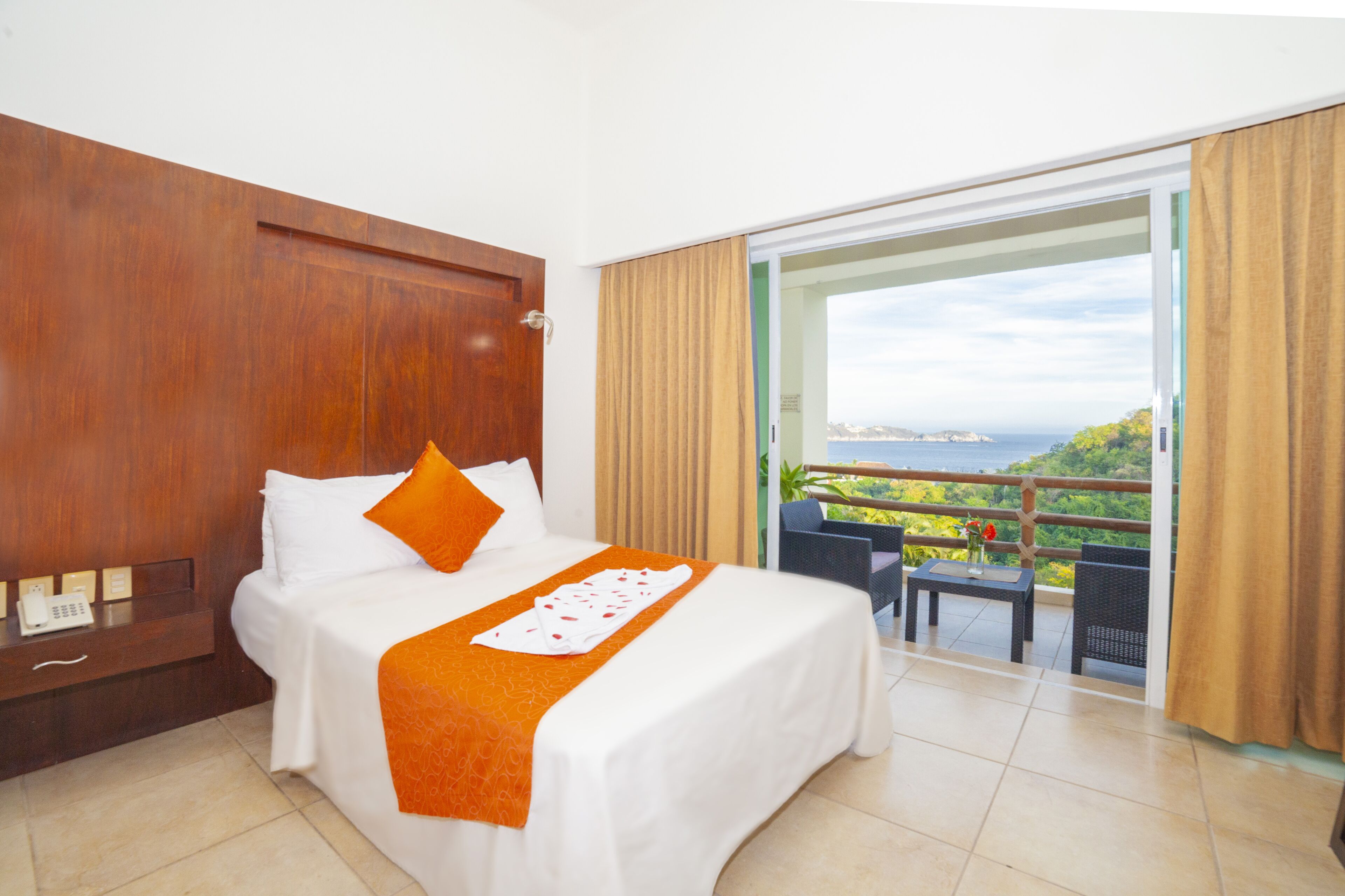 Habitación de hotel con cama, teléfono y balcón con vista al mar.