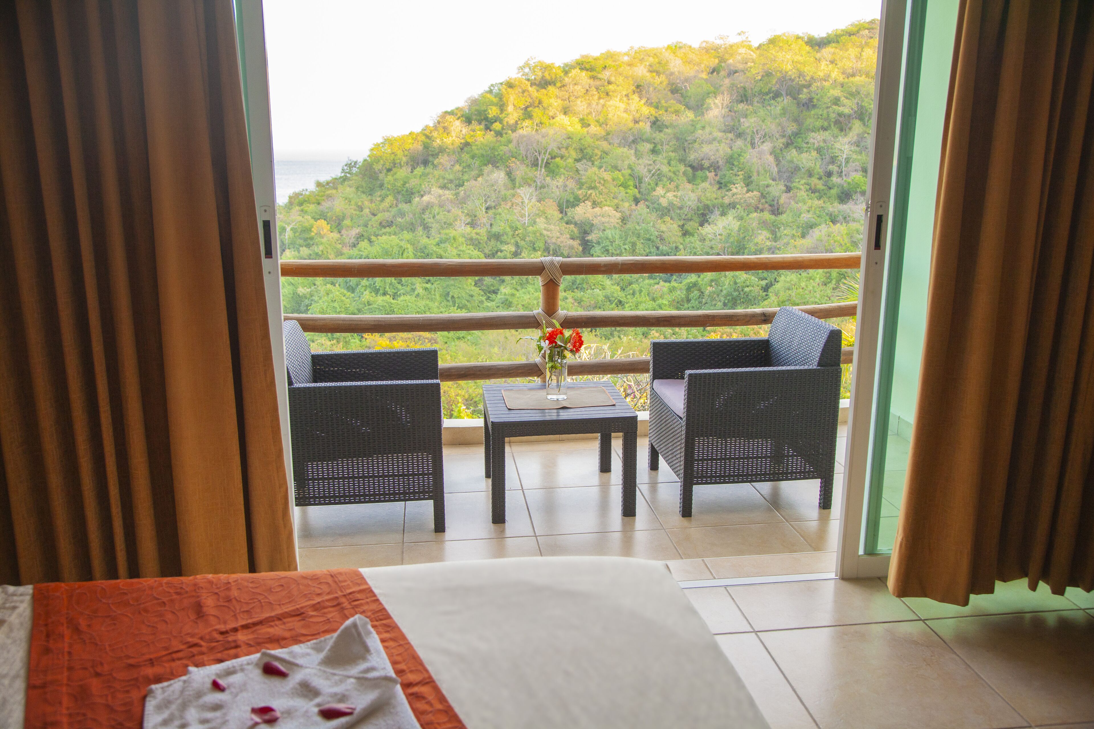 A balcony with wicker furniture and a table, overlooking a lush green hillside.