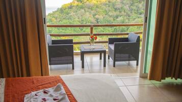 Un balcone con mobili in vimini e un tavolo, con vista su una rigogliosa collina verde.