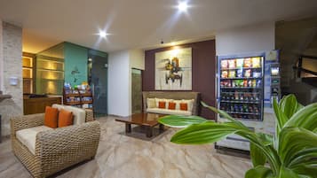 A lobby with a wicker sofa, a wooden coffee table, a vending machine, and a reception desk.