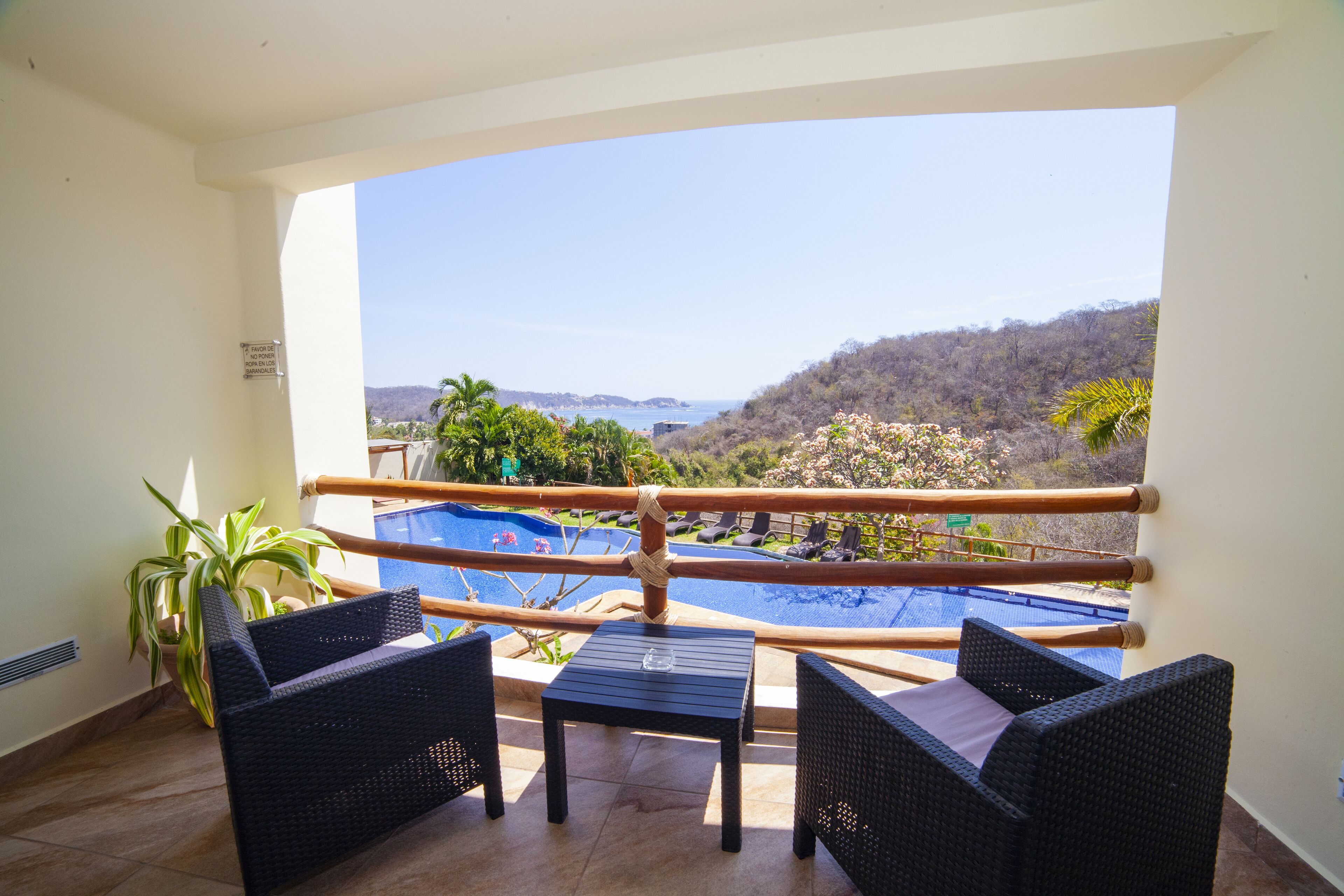 A balcony with wicker furniture, a view of a pool, and a mountainous landscape.