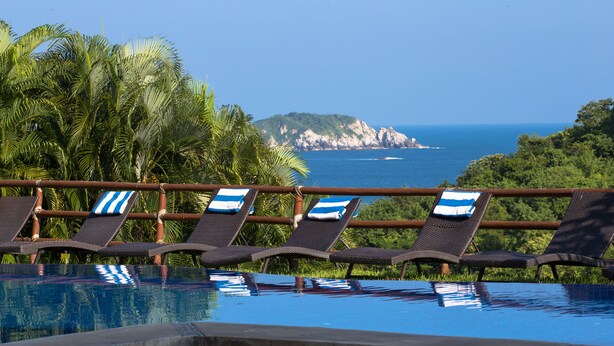 Zona de piscina con sillas de descanso y vista al océano.