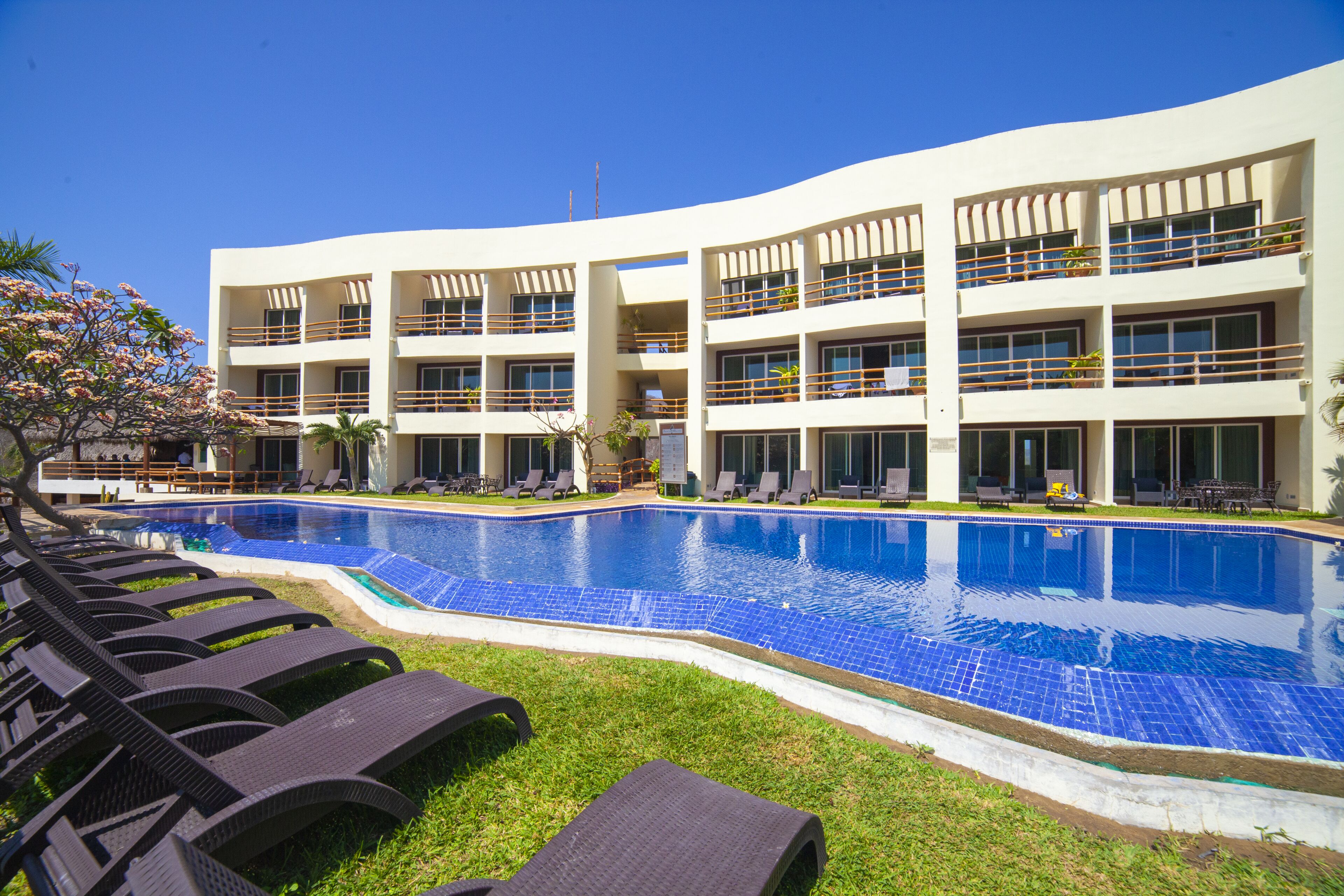 A modern hotel with a large swimming pool, multiple balconies, and outdoor seating areas.