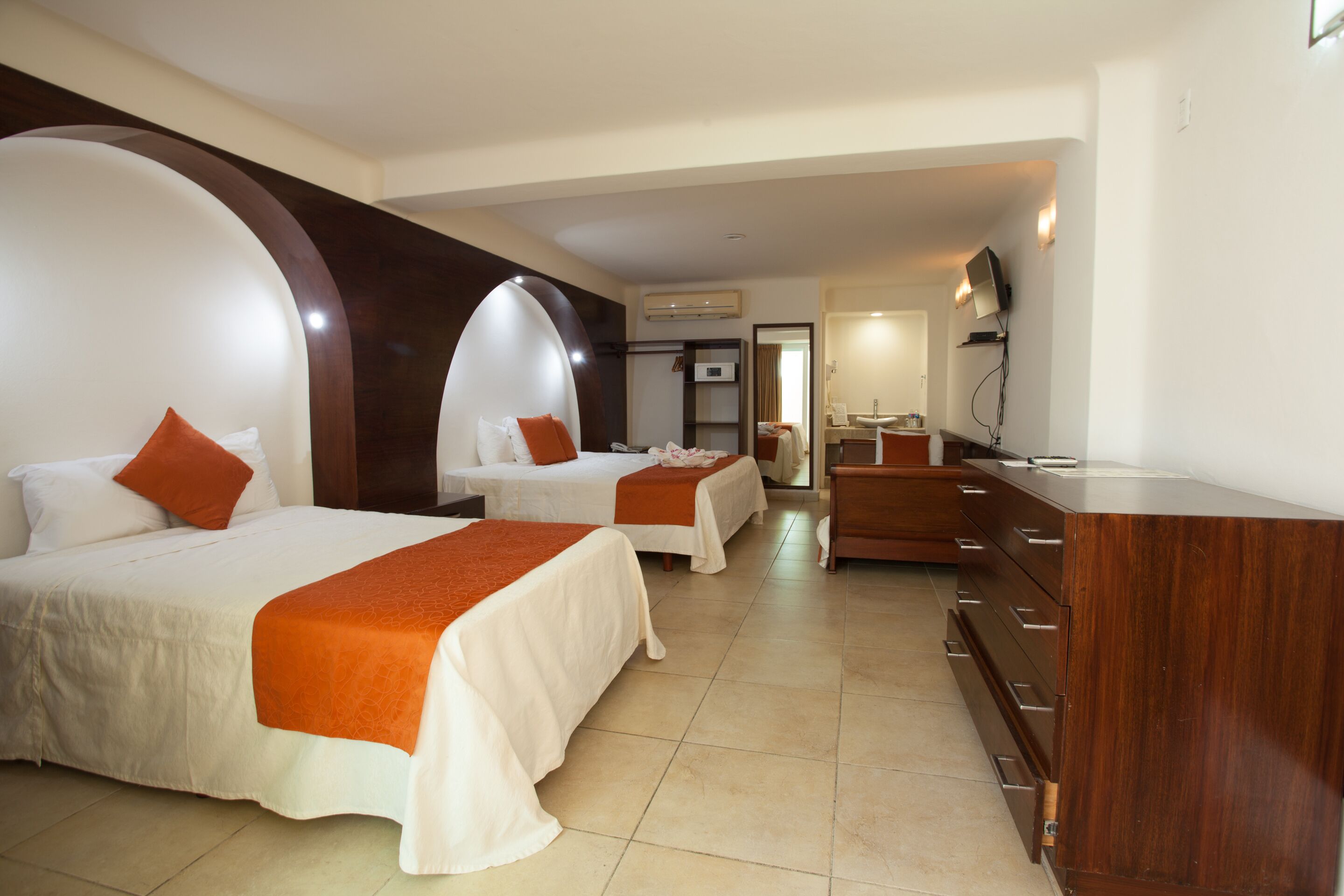 Habitación de hotel con dos camas, un aparador de madera, un escritorio y un espejo.