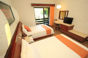A hotel room with two beds, a desk with a chair, a TV, and a balcony with a view of palm trees.