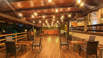 An outdoor wooden deck with wicker chairs and tables, a bar area, and a view of the night sky.