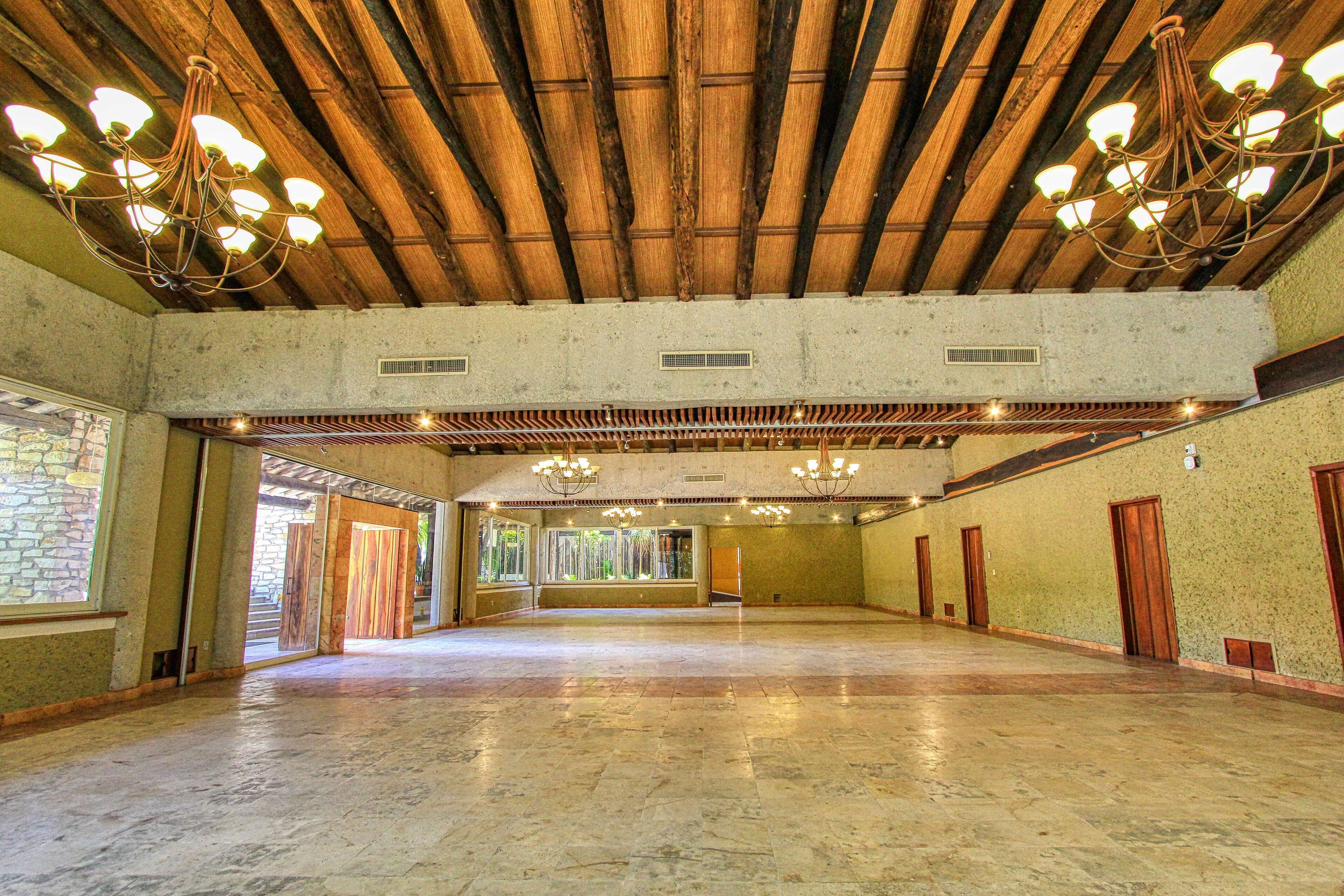 A spacious hall with a high wooden ceiling and chandeliers, large windows, and a stone wall.