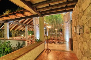 An outdoor dining area with stone walls and wooden beams, featuring tables and chairs arranged for guests. - Hotel Ciudad Real Palenque (Palenque)
