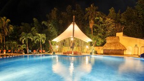 Ein Schwimmbecken mit Sonnensegel und Palmen im Hintergrund.