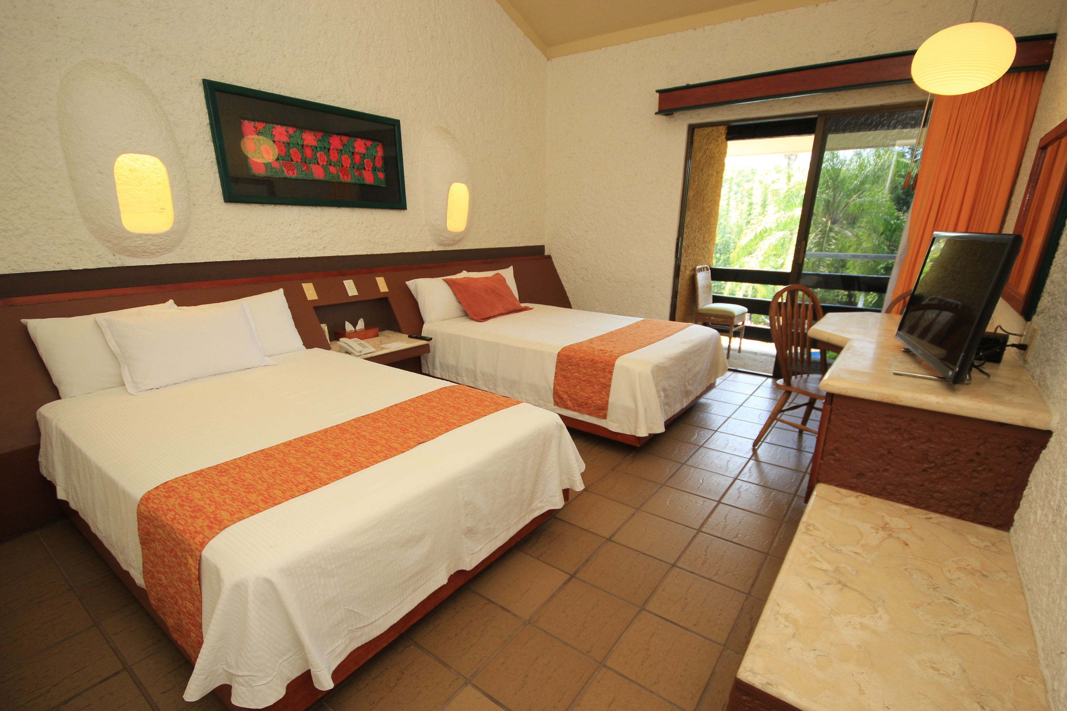 A hotel room with two beds, a desk with a computer, a chair, and a window with a view of greenery.