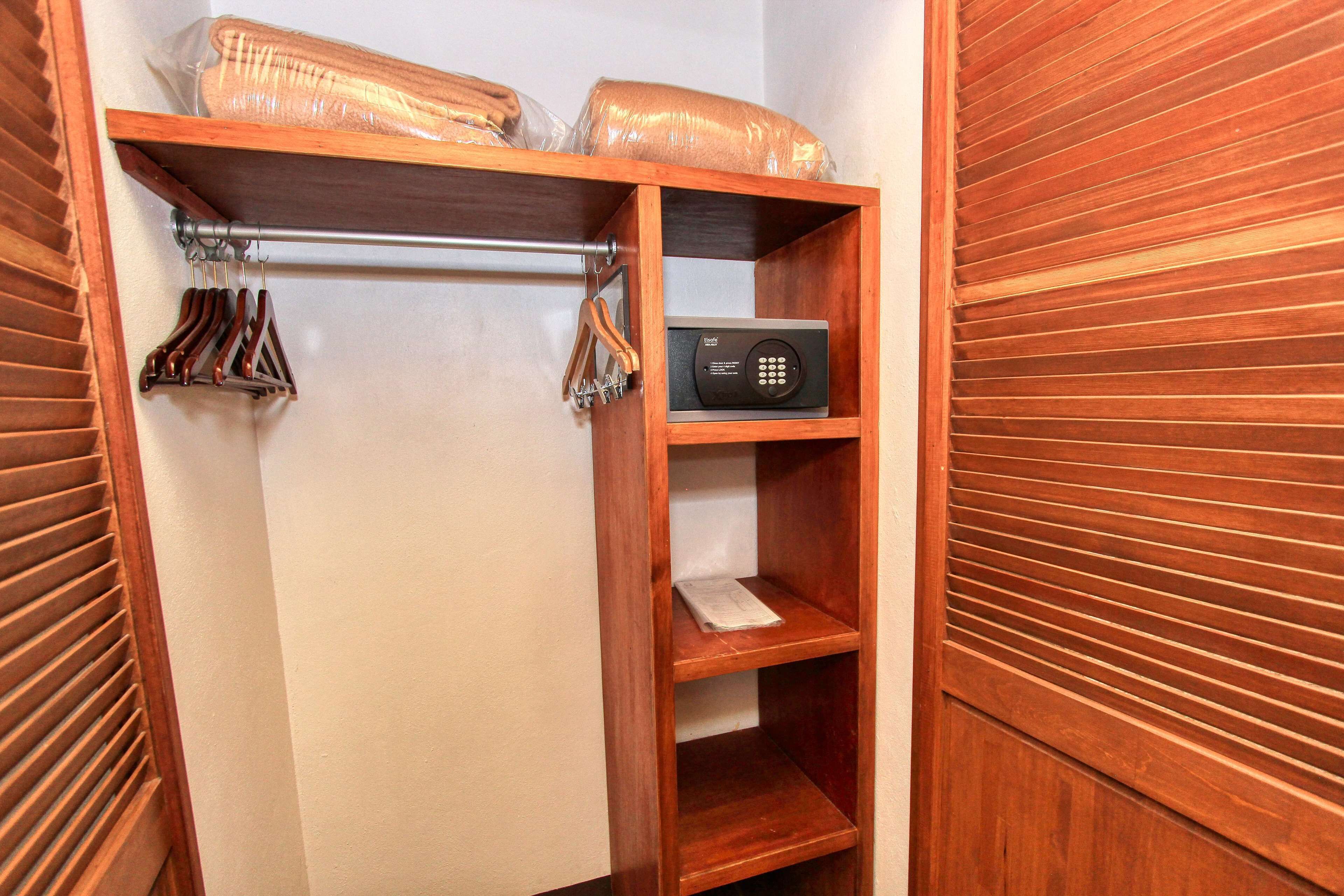 A wooden closet with shelves, a hanging rod, and a small electronic device on the top shelf.