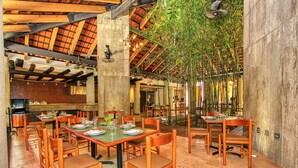 Ein Restaurant mit Holztischen und -stühlen, einer hohen Decke mit freiliegenden Balken und hängenden Bambuspflanzen.