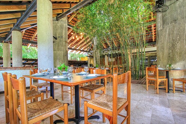 A restaurant with wooden tables and chairs, bamboo plants, and a tiled floor. - Hotel Ciudad Real Palenque (Palenque)