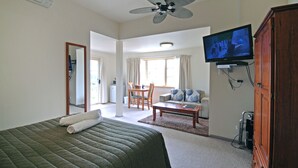 A hotel room with a bed, a television, a wooden cabinet, a ceiling fan, and a dining area with a table and chairs. - Riverview Boutique Motel (Nambucca Heads)