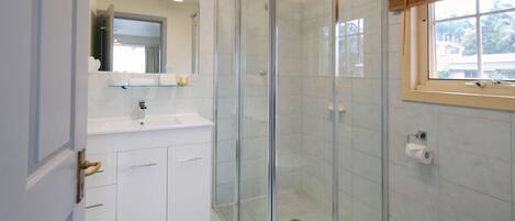 Un baño moderno con cabina de ducha de vidrio, un lavabo blanco y un inodoro.
