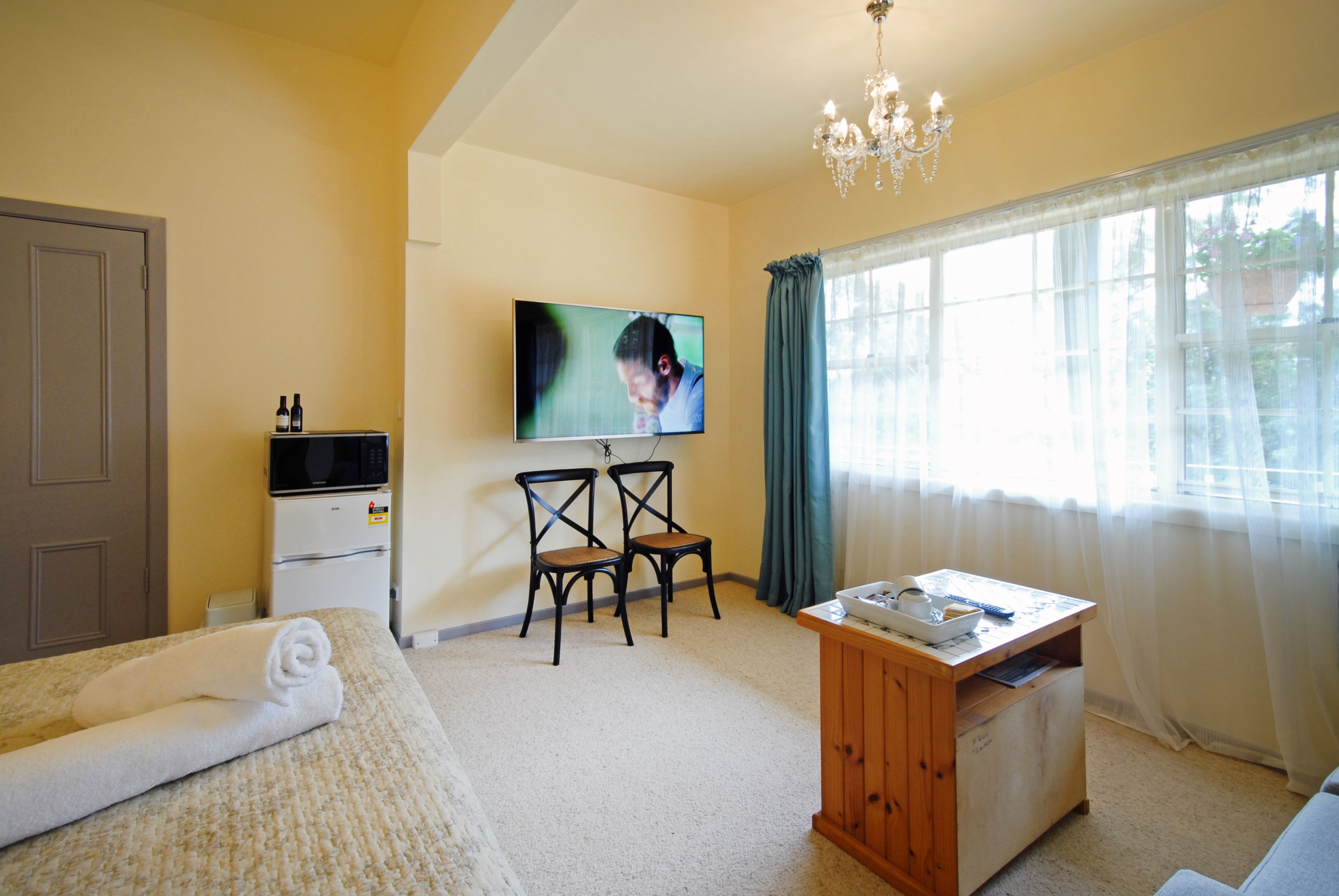 Habitación de hotel con cama, escritorio, dos sillas, televisor y ventana con cortinas.