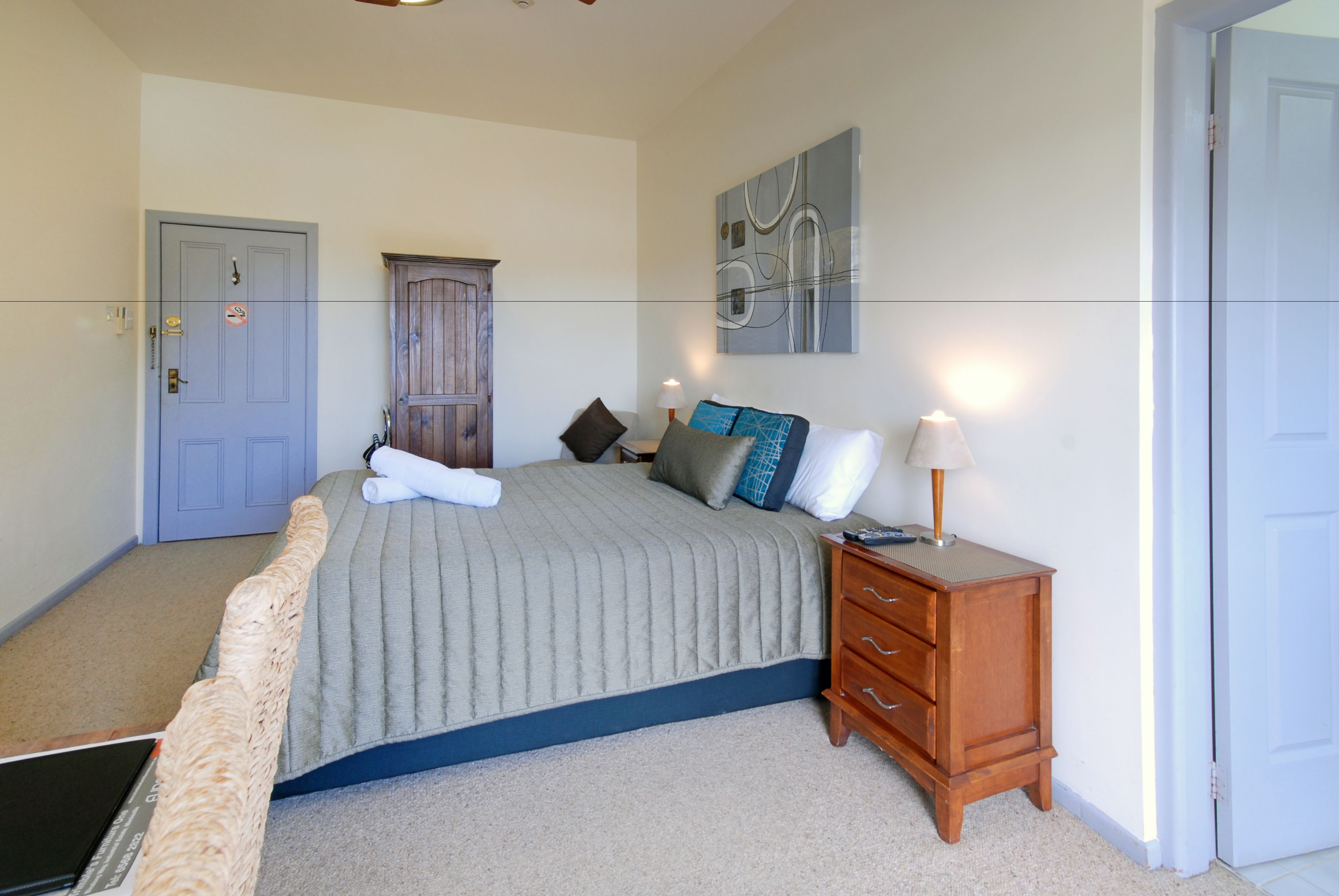 A bedroom with a bed, a wooden dresser, a nightstand, a wall art piece, and a door.