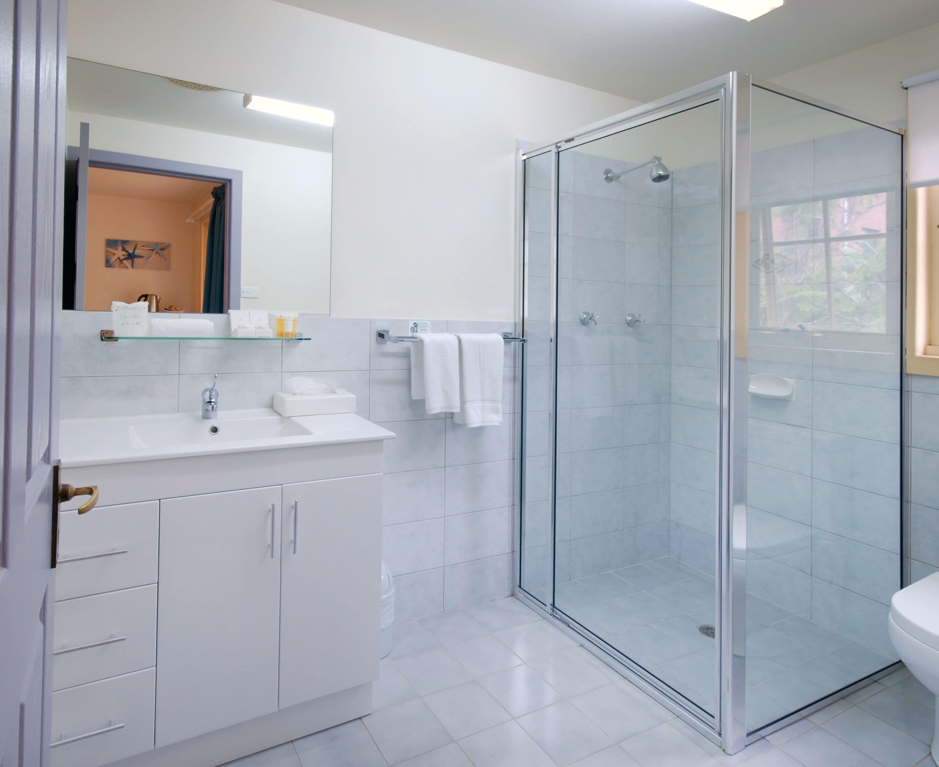 A modern bathroom with a glass-enclosed shower, white cabinetry, and a large mirror above the sink.