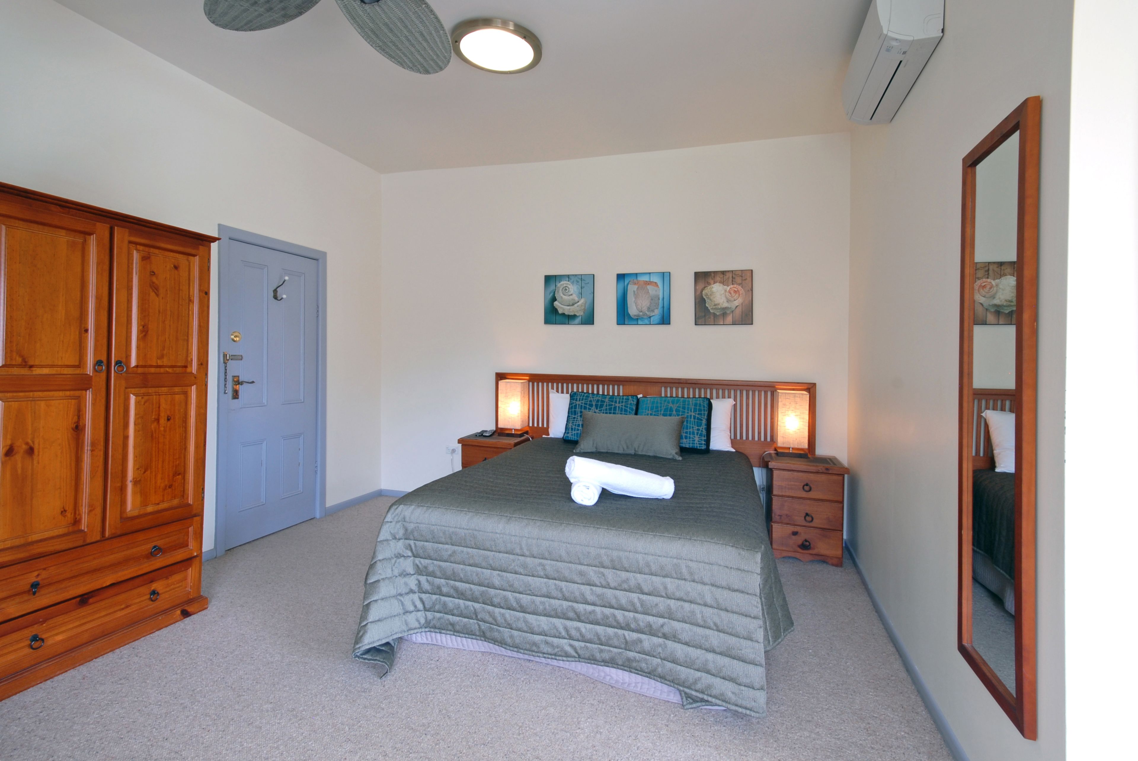A bedroom with a large bed, wooden wardrobe, and a mirror.