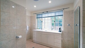 A bathroom with a marble wall, a sink with a window above, and a shower area. - Riverview Boutique Motel (Nambucca Heads)