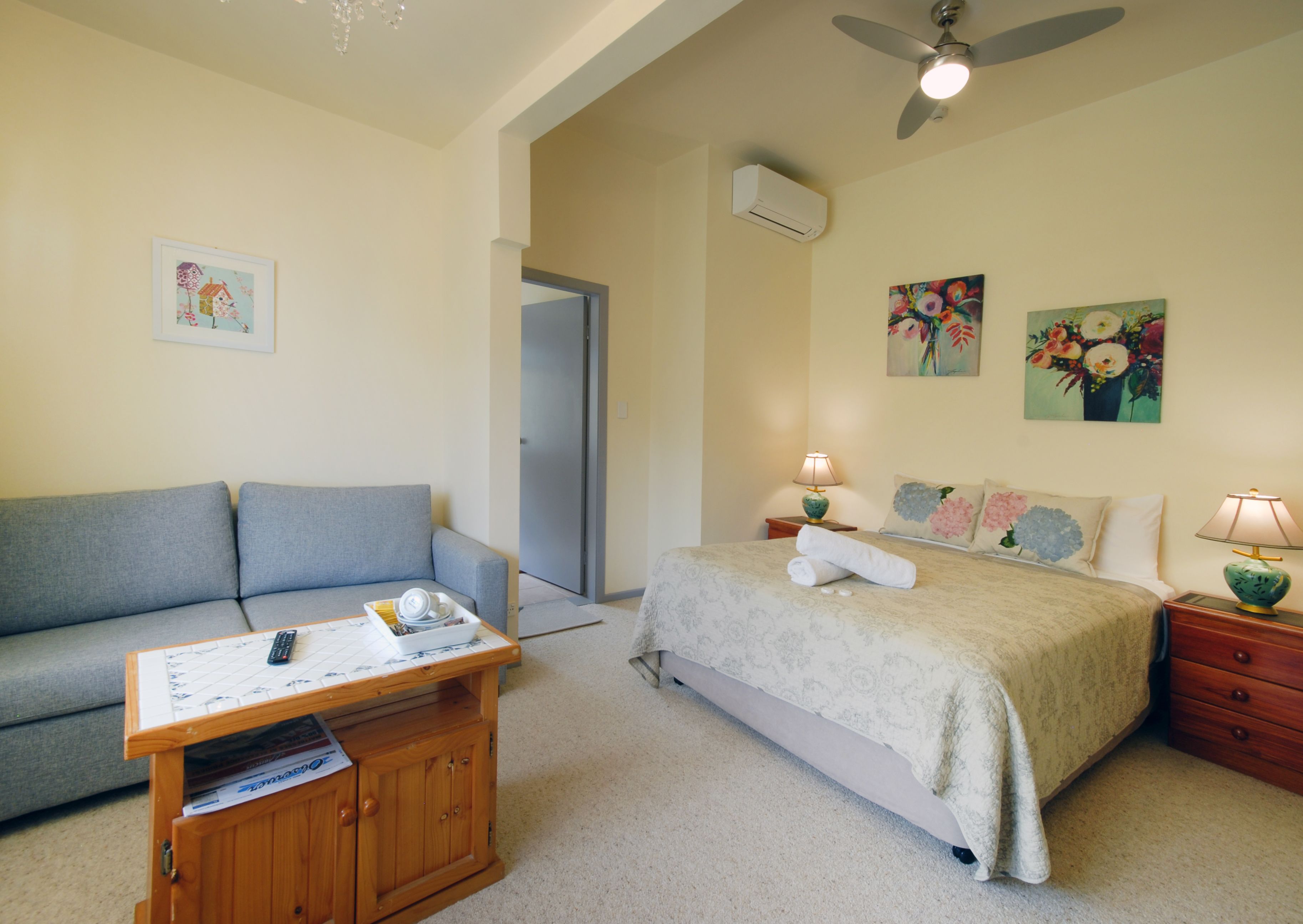 A bedroom with a bed, a sofa, a wooden cabinet, a ceiling fan, and artwork on the walls.