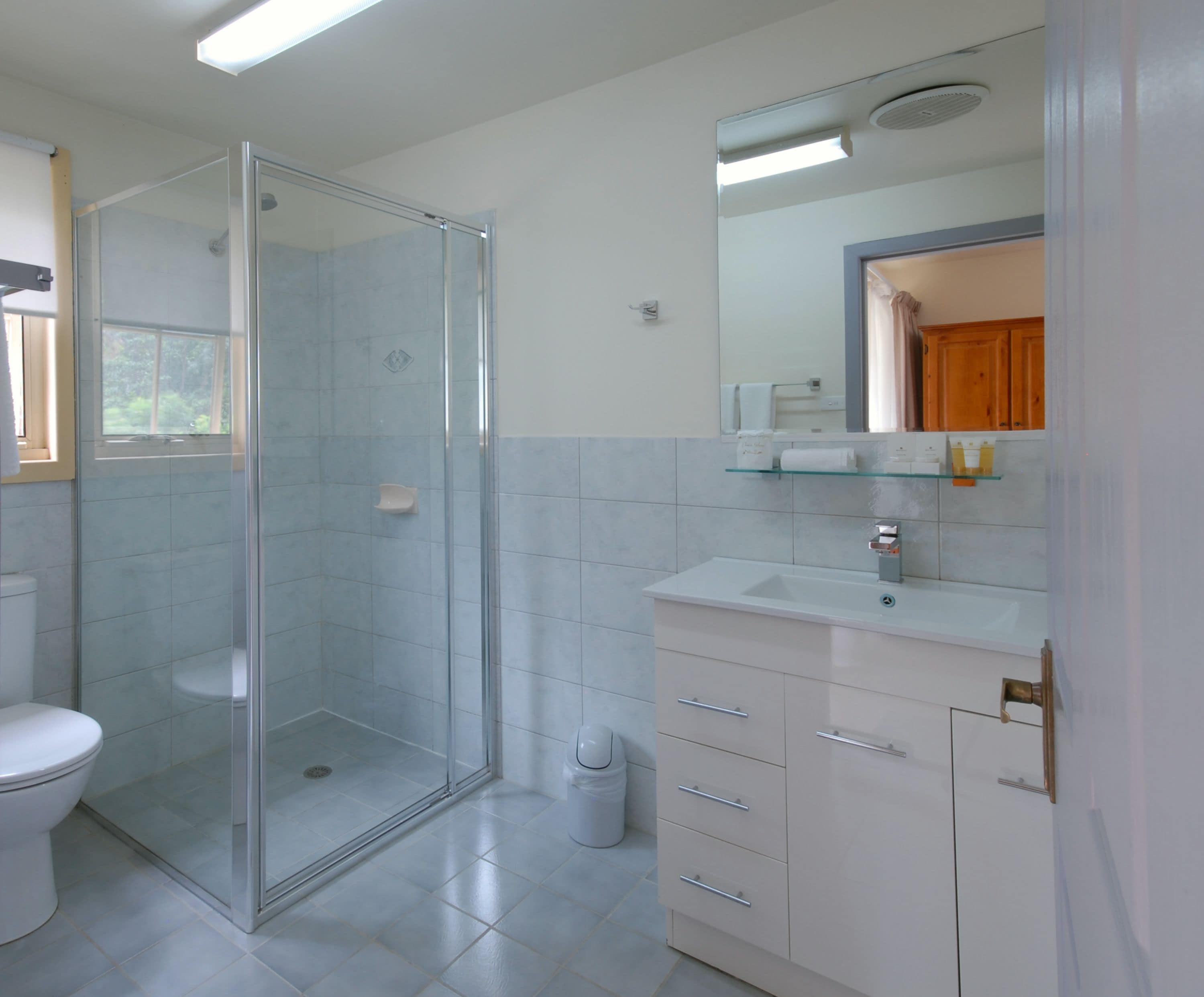 A modern bathroom with a glass-enclosed shower, a white sink with a mirror above it, and a white toilet.