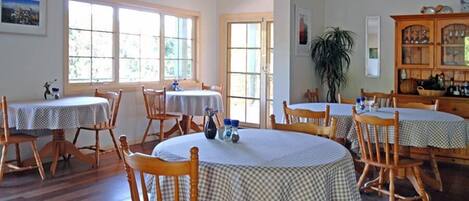A dining area with round tables and wooden chairs, large windows, and a cabinet with glass doors.