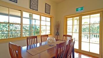 A dining area with a wooden table and chairs, large windows with a view of greenery, and decorative wall art.