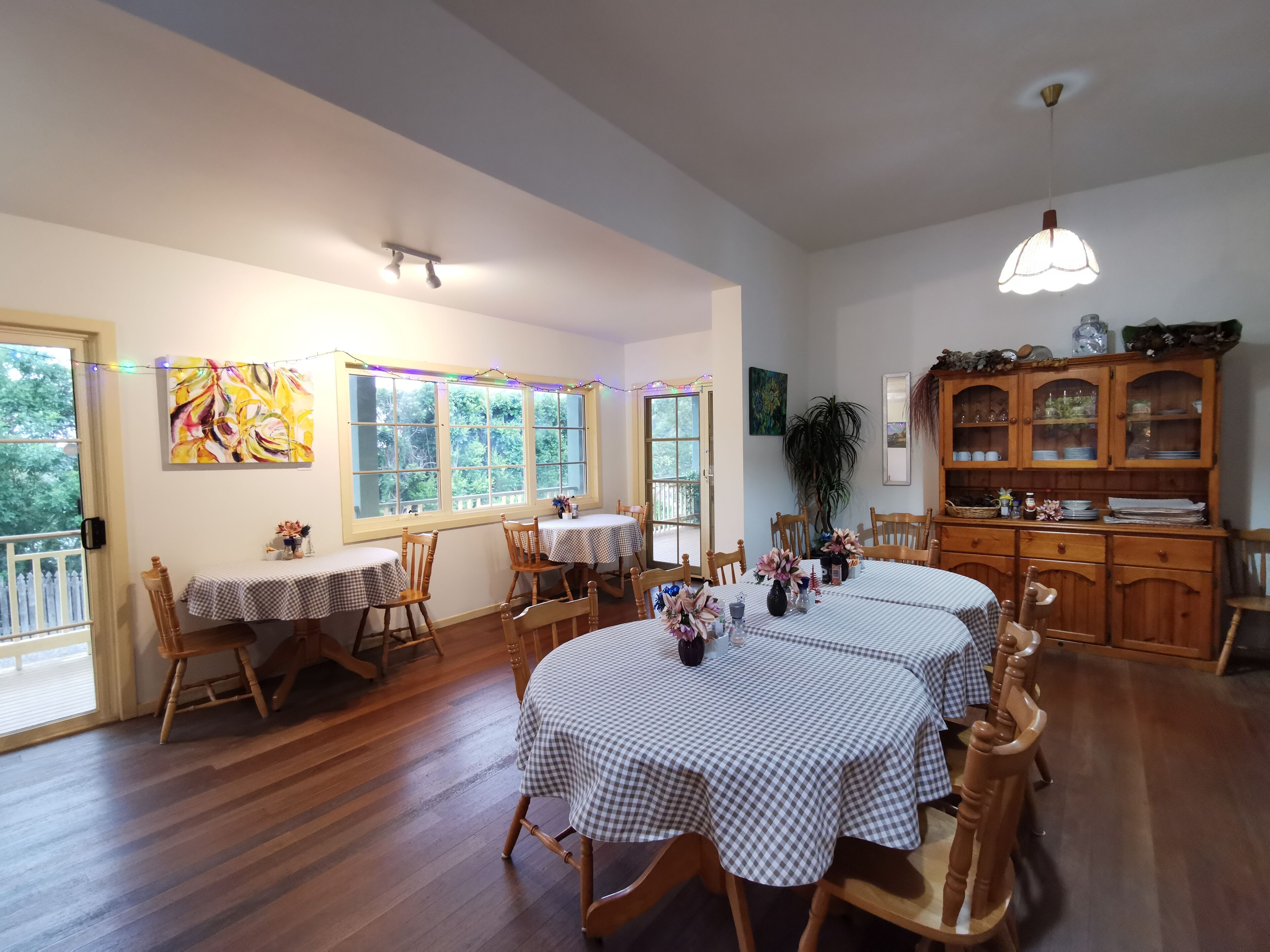 Un comedor con manteles a cuadros, sillas de madera y un amplio ventanal con vistas a árboles.