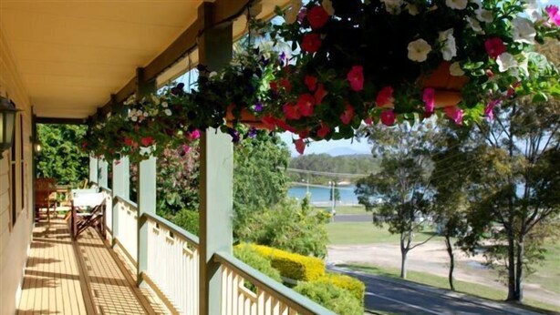 A wooden deck with hanging flower baskets, a view of a lake, and a well-maintained lawn. - Riverview Boutique Motel (Nambucca Heads)