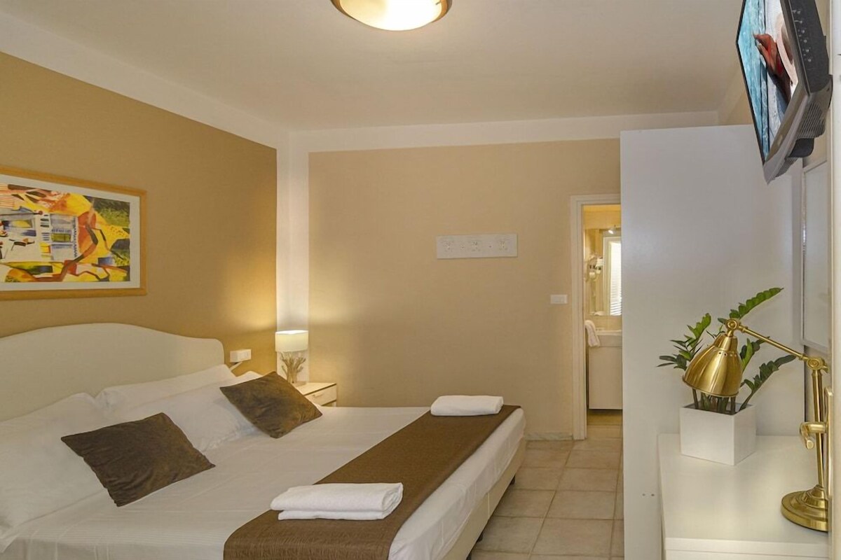 A hotel room with a bed, bedside tables, a lamp, and a television.