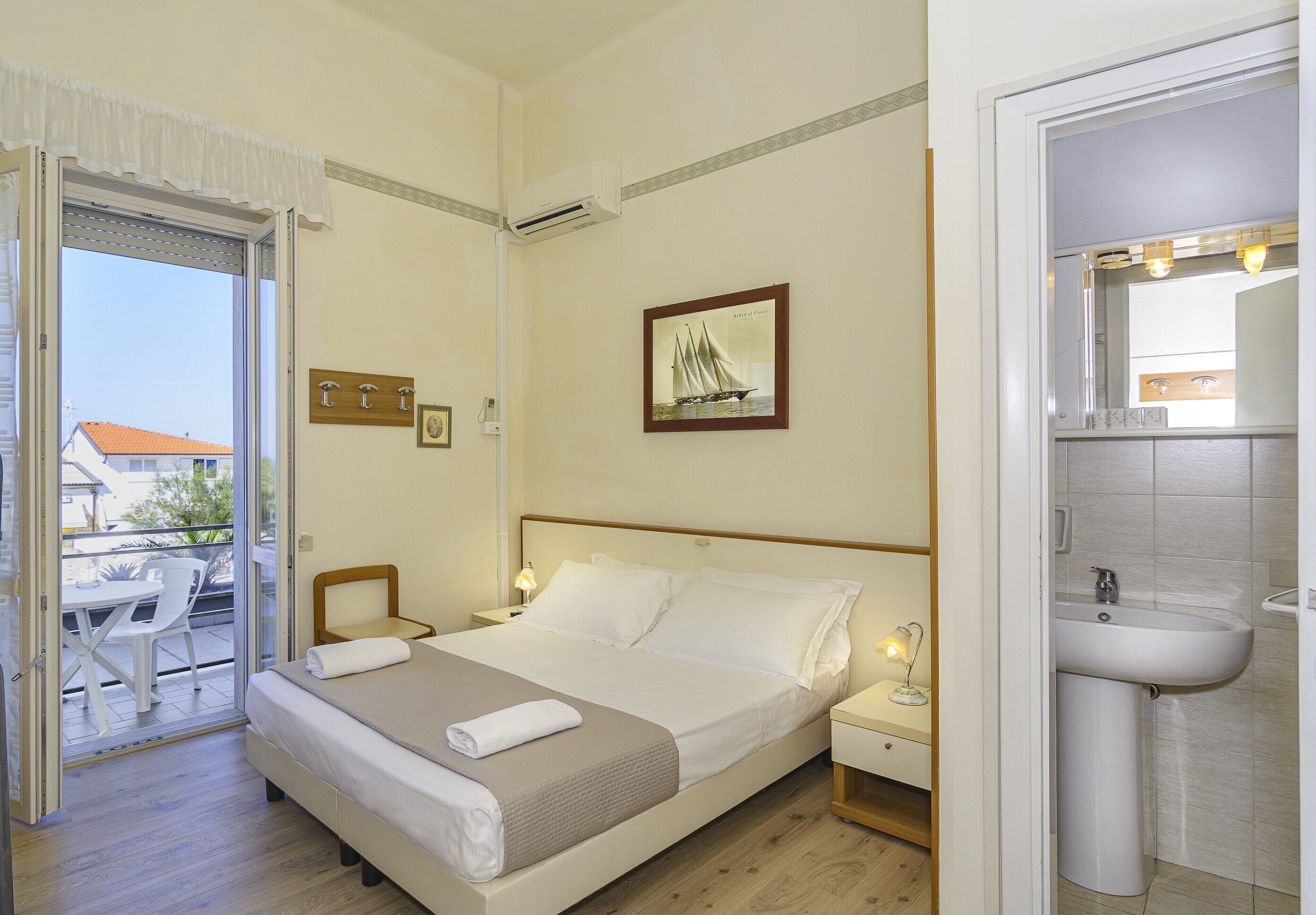 Habitación de hotel con cama, mesita de noche con lámpara, ventana con vistas al exterior y baño con lavabo y espejo.