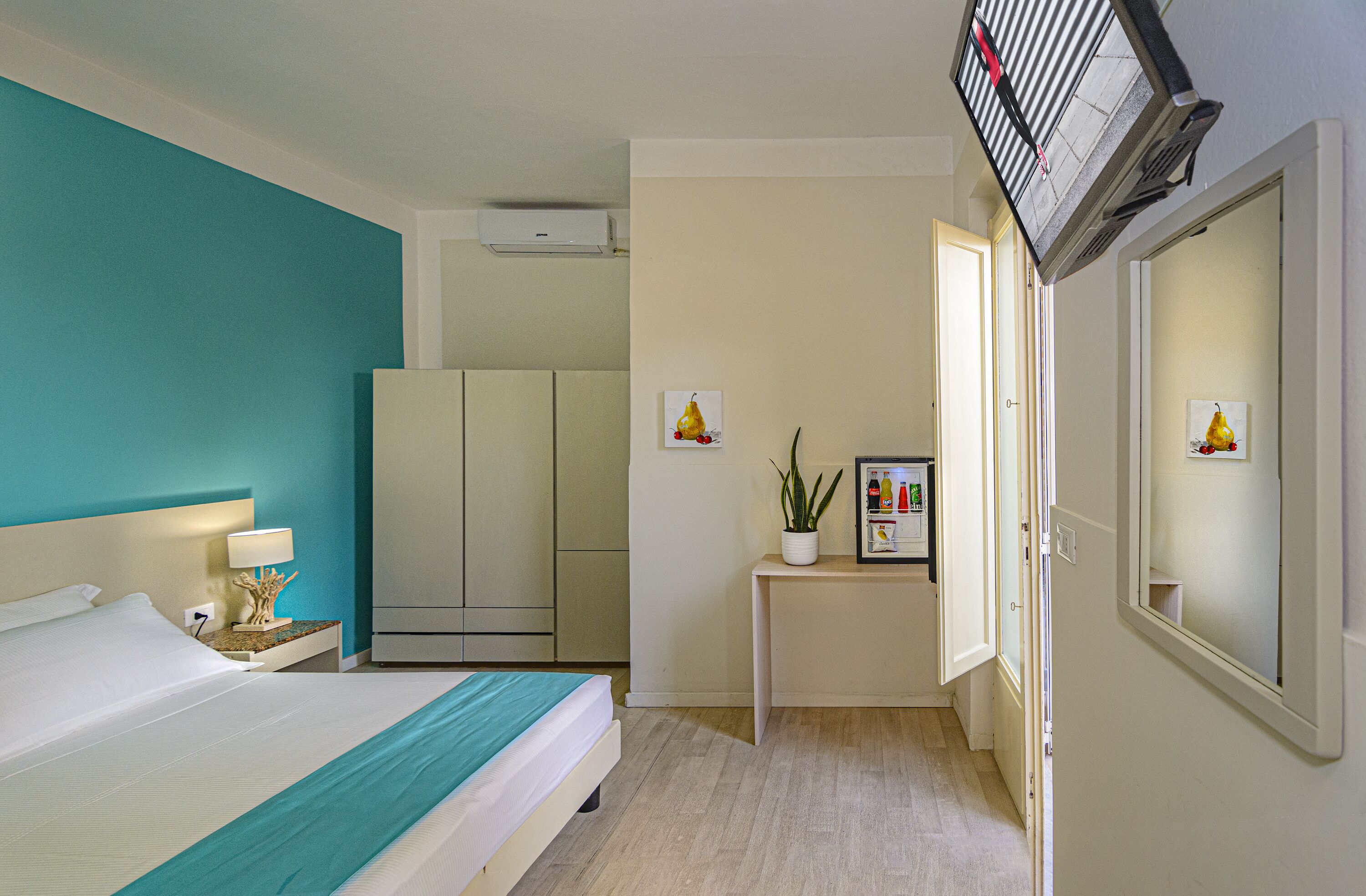 Habitación de hotel con cama, escritorio, espejo y puerta que da a un baño.