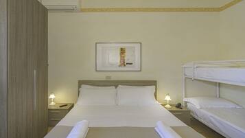 Una camera d'albergo con un letto singolo, una cuccetta, un comodino con una lampada e un quadro appeso al muro.