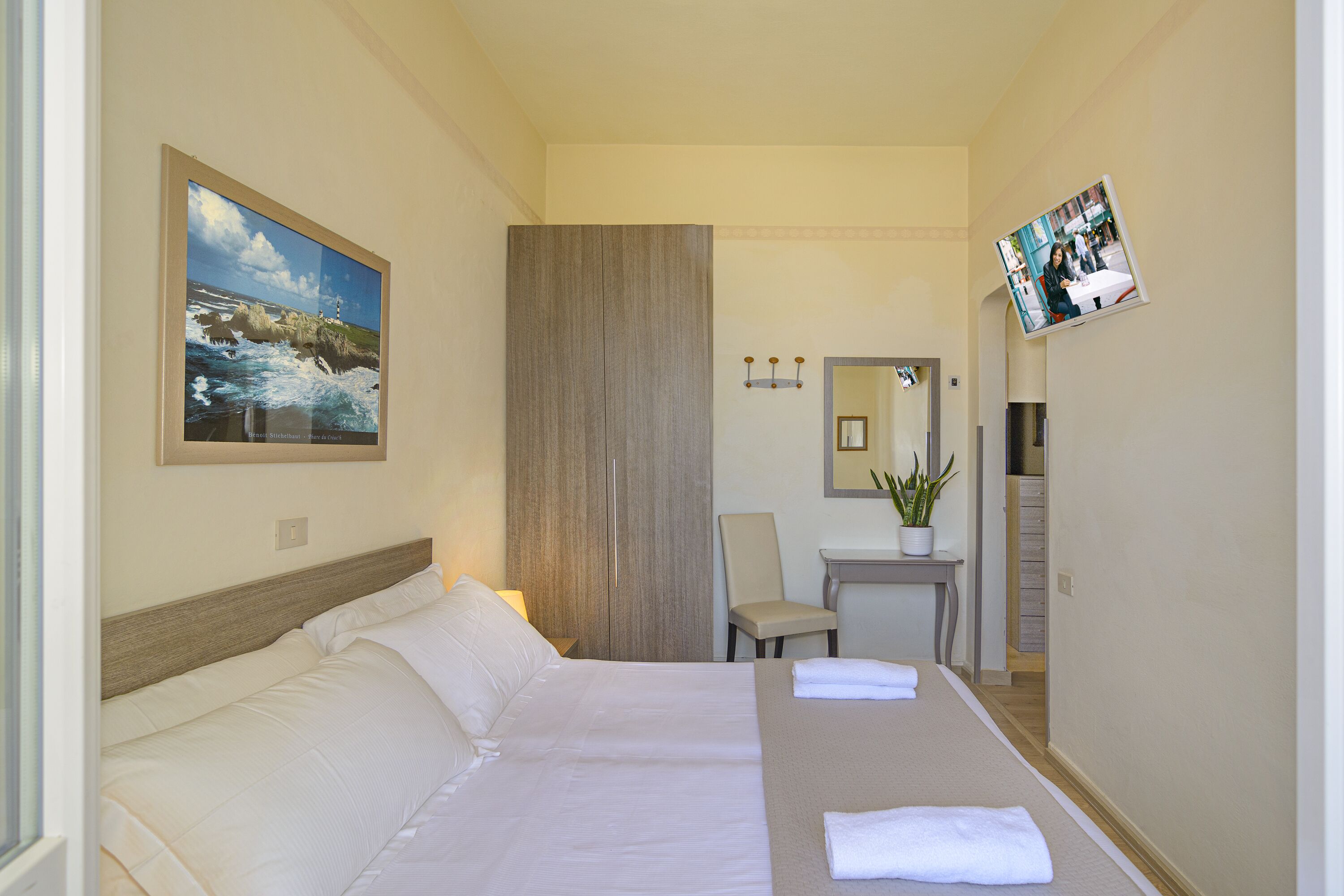 Una habitación de hotel con cama, escritorio, silla, televisión y un cuadro en la pared.