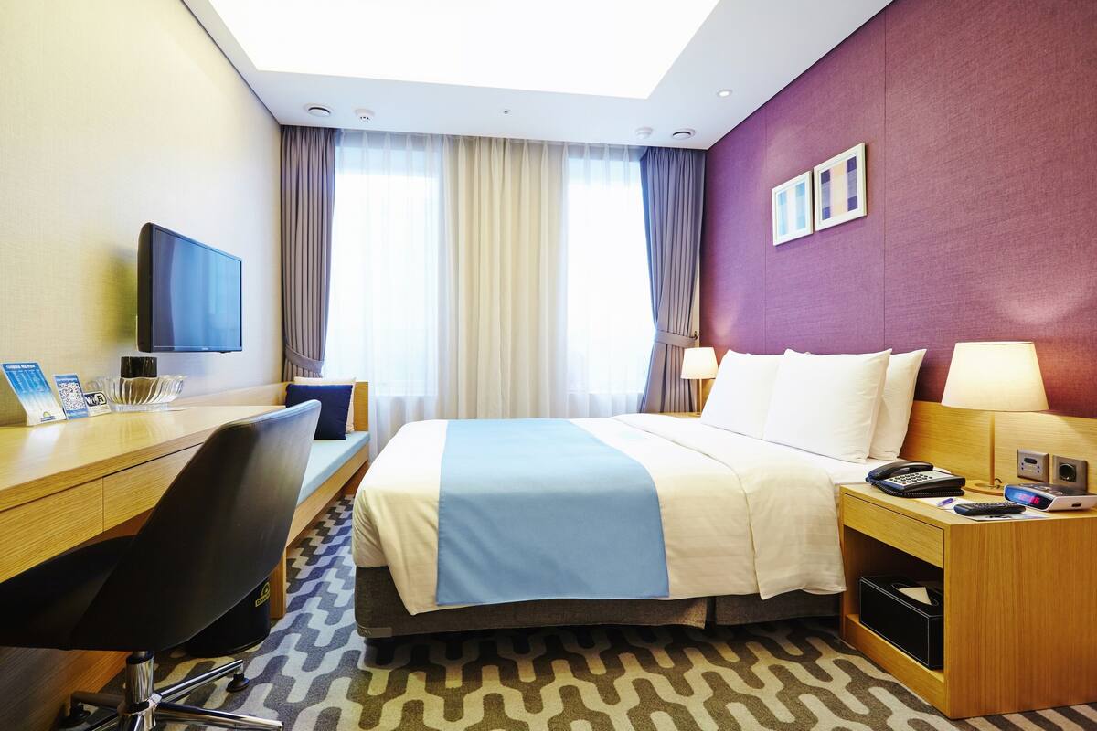 A hotel room with a bed, desk, chair, television, and a window with curtains.