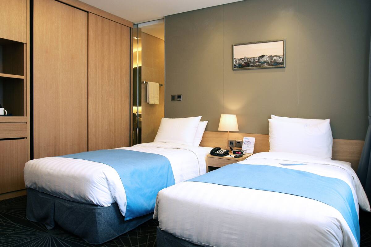 A hotel room with two beds, a nightstand with a lamp, a phone, and a picture on the wall.