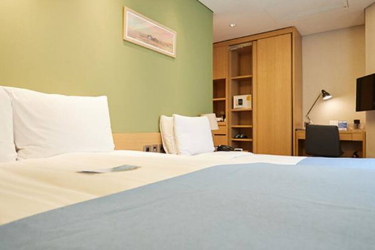A hotel room with a bed, a desk, a chair, a lamp, and a television.