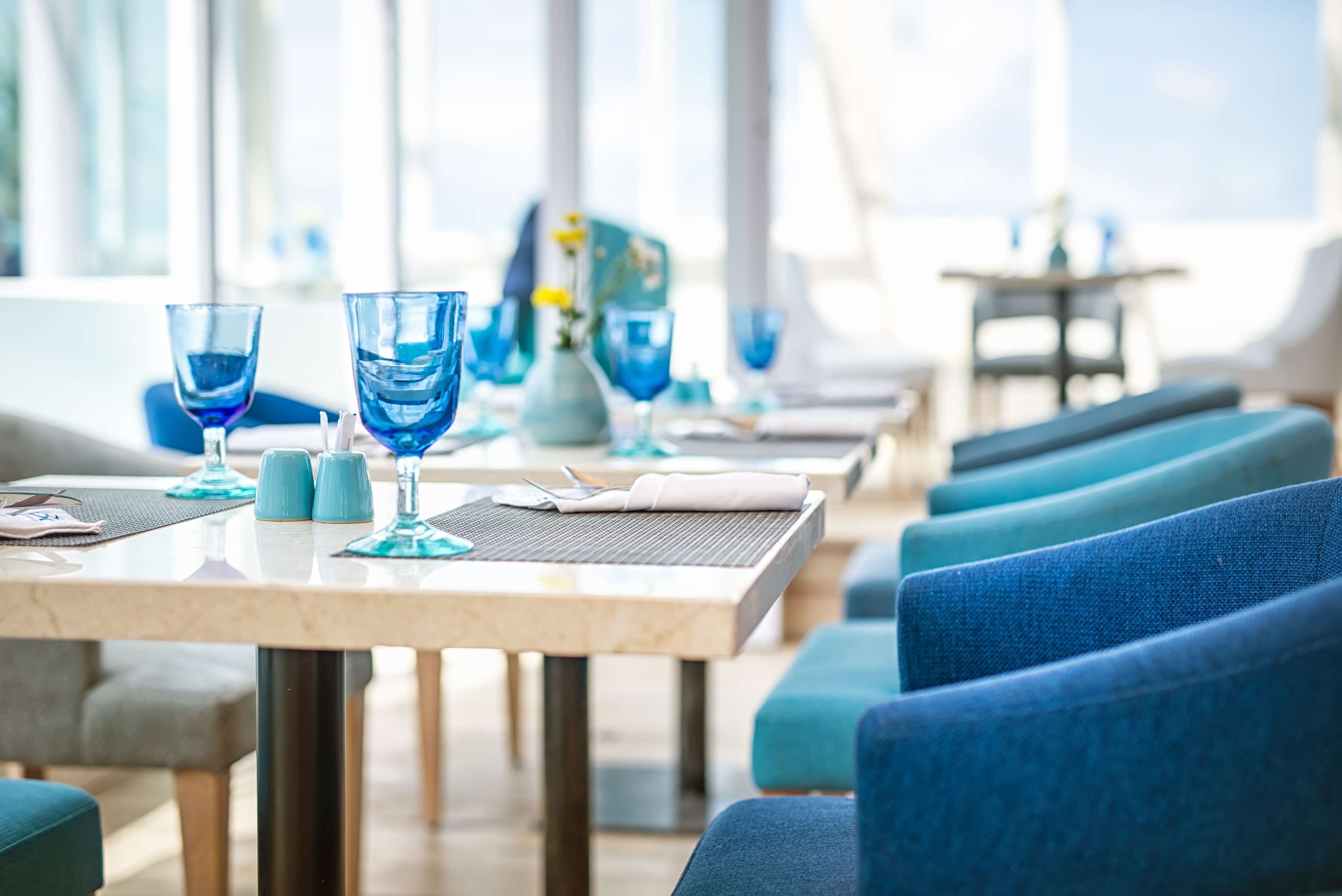 Un comedor con sillas tapizadas en azul, una mesa de mármol y cristalería azul.